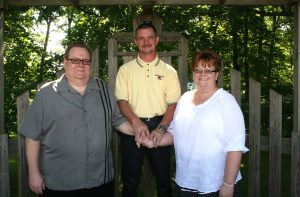 Photo of Rick Gardner standing in the center, with his hands uniting Paul and Debbie Oyler.